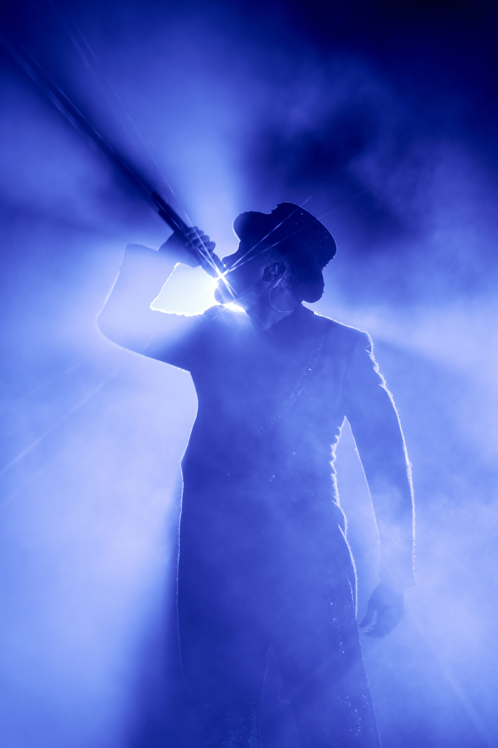 L&iacute;o Mykonos: One Last Spectacularrr Night. A singer holding a microphone amid blue light and stage haze.