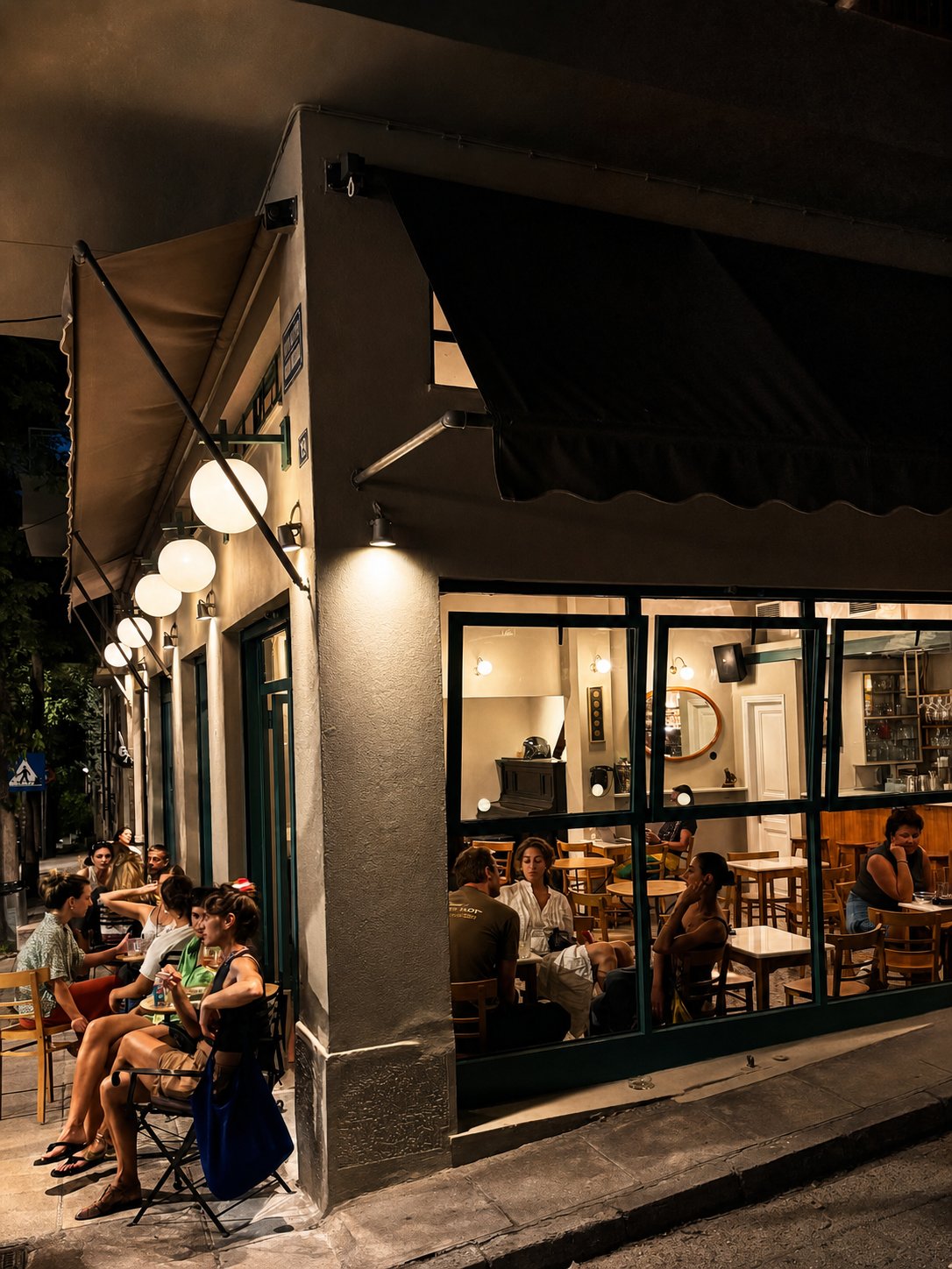 Pangrati and Mets walk: Odeon caf&eacute;-bar at night, with customers sitting at tables along its corner frontage.